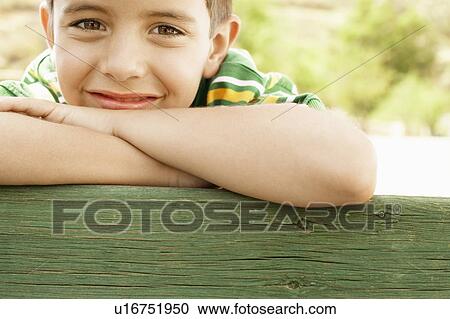 Stock Image - Boy (7-9) leaning on railing, close-up portrait.. Fotosearch