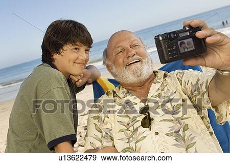 Boy and grandfather photographing themselves on beach View Large Photo Image Stock Photo - Boy and grandfather photographing themselves on beach. Fotosearch
