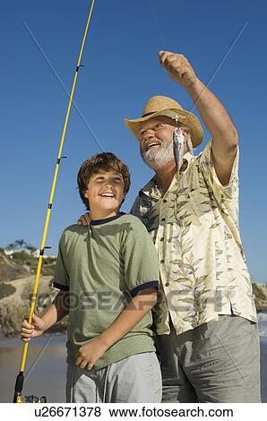 Stock Photo - Boy and grandfather showing off fish on beach. Fotosearch