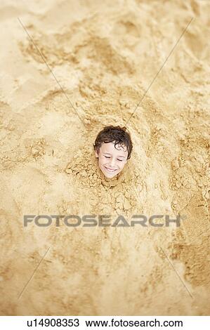Stock Image - Boy buried in sand to his neck, view from above. Fotosearch