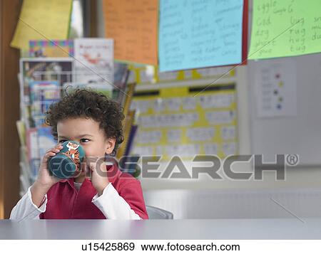 Stock Photo - Boy drinking from cup in classroom. Fotosearch