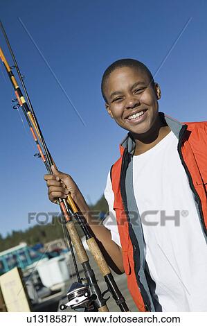 Stock Image - Boy holding fishing rod, smiling, (portrait). Fotosearch