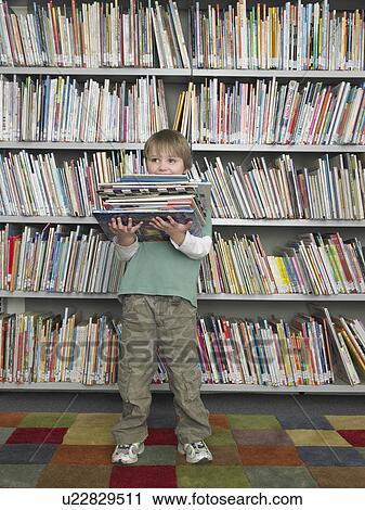 Boy holding stack of books in front of library bookshelf View Large Photo Image Stock Image - Boy holding stack of books in front of library bookshelf. Fotosearch