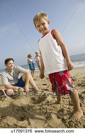Stock Photograph - Boy Playing in Sand with Family at Beach. Fotosearch