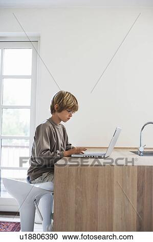 Stock Image - Boy using laptop at kitchen table. Fotosearch