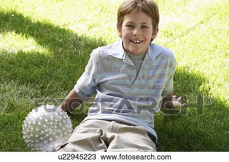 Boy with ball sitting on park lawn, portrait View Large Photo Image Stock Image - Boy with ball sitting on park lawn, portrait. Fotosearch