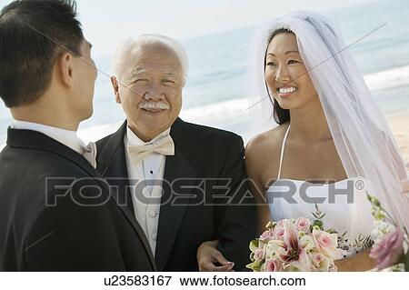 Stock Photo - Bride and father arm in arm with groom at beach wedding. Fotosearch