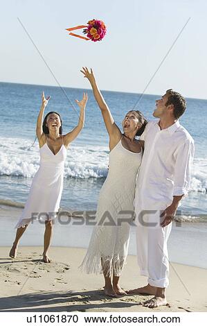 Stock Image - Bride throwing bouquet on beach. Fotosearch