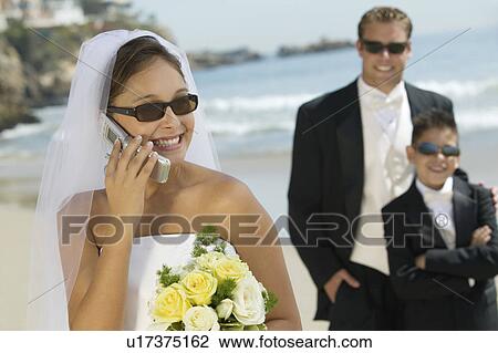 Stock Image - Bride using mobile phone, Groom and brother in background. Fotosearch