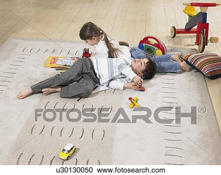 Stock Image - Brother and sister (3-6) laying on rug in home. Fotosearch