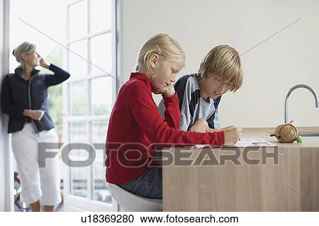 Stock Image - Brother and Sister Doing Homework in kitchen. Fotosearch