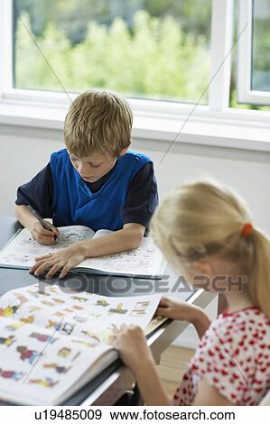 Stock Photo - Brother and sister reading books at table at home. Fotosearch