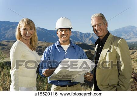 Stock Photograph - Builder with couple and blueprint for new home, portrait. Fotosearch