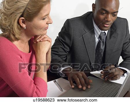 Stock Image - Business colleagues using laptop at conference table. Fotosearch