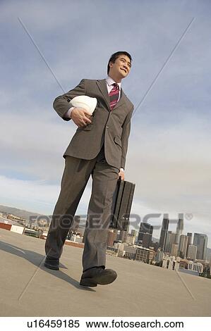 Stock Photography - Business man carrying hard hat on city rooftop. Fotosearch