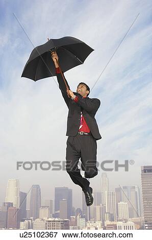 Stock Photo - Business man floating away on umbrella above city. Fotosearch
