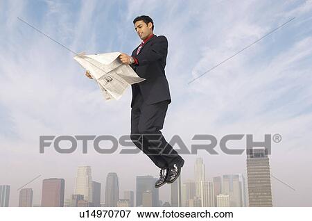 Stock Photo - Business man reading newspaper mid-air above city. Fotosearch