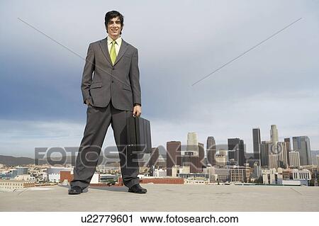 Stock Image - Business man standing on city rooftop. Fotosearch