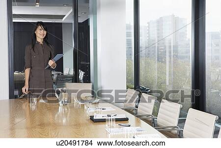Picture - Business woman standing behind table in boardroom. Fotosearch