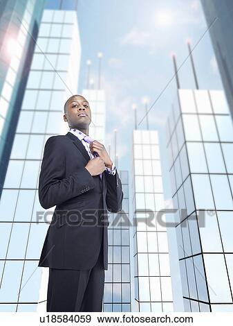 Businessman adjusting tie in front of skyscraper, digital composite View Large Photo Image Stock Photo - Businessman adjusting tie in front of skyscraper, digital composite. Fotosearch