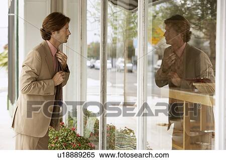 Stock Photography - Businessman adjusting tie in shop window. Fotosearch