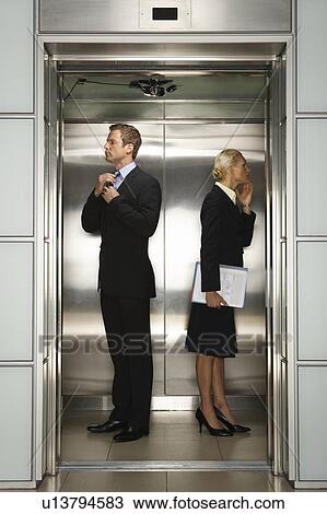 Stock Image - Businessman and Businesswoman checking their reflection in Office Elevator. Fotosearch