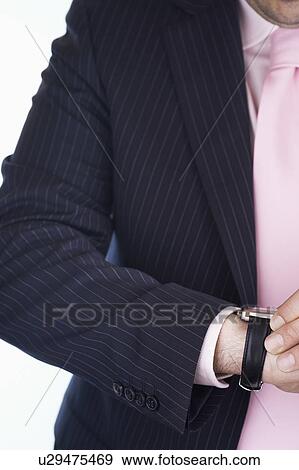 Stock Photo - Businessman checking wristwatch, mid section, close-up. Fotosearch