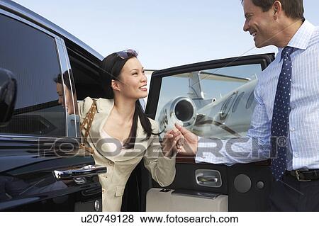 Stock Photo - Businessman helping Woman Get Out of Car parked near private jet, side view. Fotosearch
