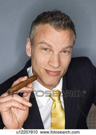 Stock Image - Businessman holding cigar in studio. Fotosearch