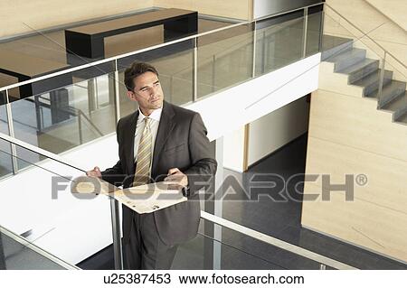 Stock Image - Businessman holding newspaper standing on Mezzanine. Fotosearch