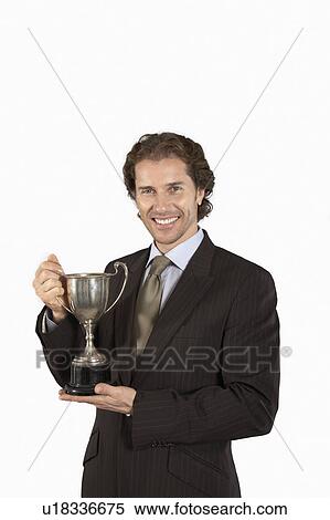 Stock Photography - Businessman holding trophy, smiling, on white background, portrait. Fotosearch
