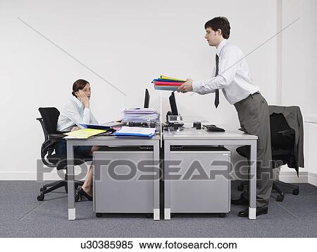Stock Photography - Businessman passing off work to female colleague in office. Fotosearch