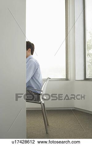 Stock Image - Businessman sitting on chair in office, side view, obscured face. Fotosearch