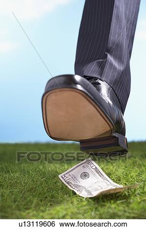 Stock Photograph - Businessman stepping on fifty-dollar bill in grass, close-up of foot. Fotosearch