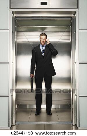 Stock Image - Businessman Using Cell Phone on Elevator, front view. Fotosearch