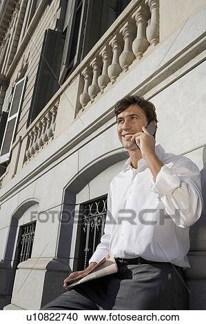 Stock Image - Businessman using mobile phone by high-rise building. Fotosearch