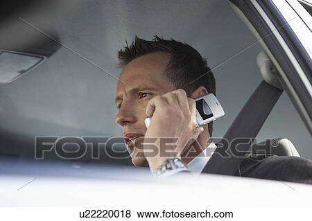 Stock Photo - Businessman using mobile phone in car, low angle view. Fotosearch