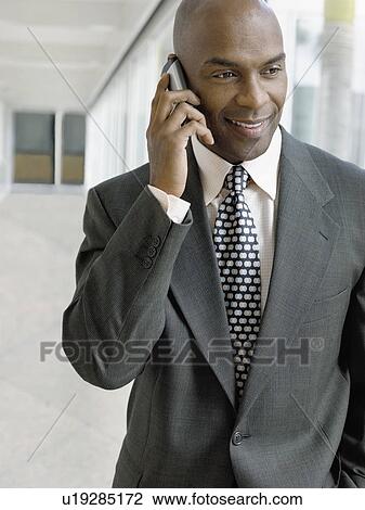 Stock Image - Businessman using mobile phone in hallway. Fotosearch