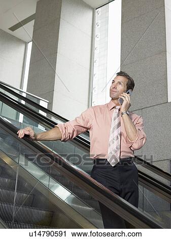 Stock Image - Businessman using mobile phone on escalator. Fotosearch