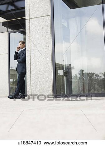 Businessman using mobile phone outside office building View Large Photo Image Stock Image - Businessman using mobile phone outside office building. Fotosearch