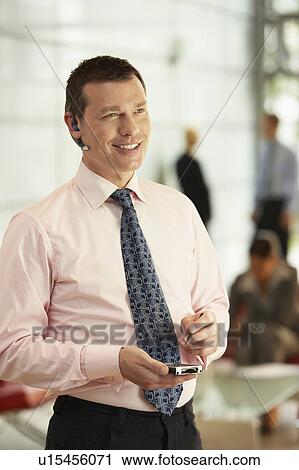 Stock Image - Businessman Using Wireless Headset and PDA in office. Fotosearch