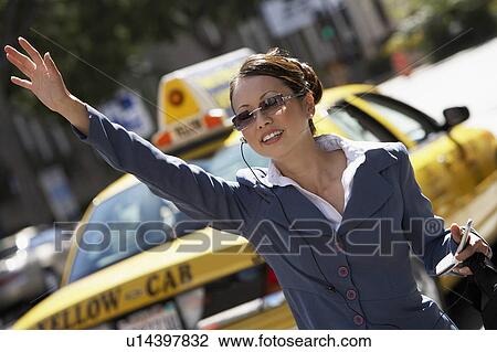 Stock Image - Businesswoman Hailing Cab using Cell Phone with hands free. Fotosearch