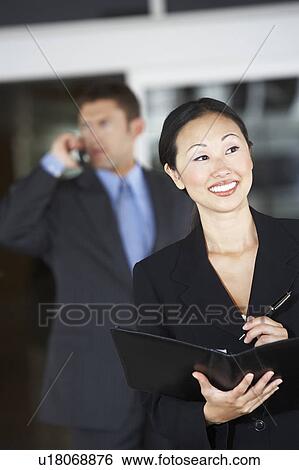 Businesswoman holding folder in front of businessman using phone View Large Photo Image Stock Photograph - Businesswoman holding folder in front of businessman using phone. Fotosearch