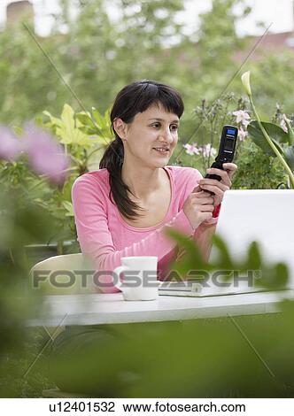 Stock Image - Businesswoman looking happily at Cell Phone with white laptop in garden. Fotosearch