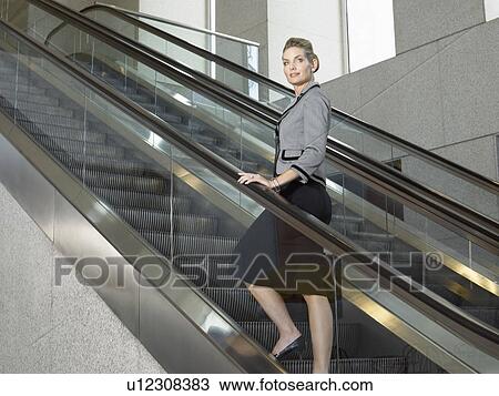 Stock Image - Businesswoman on escalator, (portrait). Fotosearch