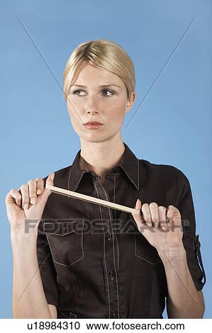 Stock Image - Businesswoman stretching rubber band, on blue background, portrait. Fotosearch