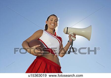 Stock Photo - Cheerleader Holding Football and Megaphone, low angle view, portrait, (portrait), (low angle view). Fotosearch