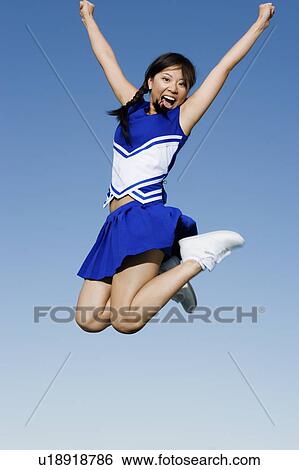 Stock Photograph - Cheerleader jumping in mid-air, ), (low angle view). Fotosearch