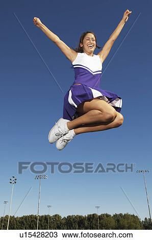Stock Image - Cheerleader jumping, mid air, low angle view, (low angle view). Fotosearch