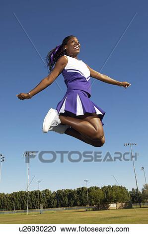 Stock Image - Cheerleader jumping on field, mid air, low angle view, (low angle view). Fotosearch